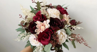 A hand holds a beautiful bouquet of engagement flowers with deep red and white roses, as seen in a floral guide for Calgary.