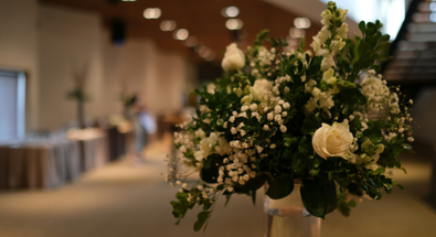 A close-up of an elegant corporate event floral centerpiece with white roses and baby's breath, set against the blurred background of a professionally arranged event hall.